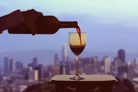 A glass of red wine being poured, with the 威尼斯人官网平台app skyline visible out the window.